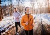 Two people jogging in a snowy forest path