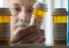 An elderly man holding a prescription bottle while examining it closely