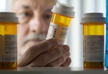 An elderly man holding a prescription bottle while examining it closely