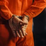 Rural Horror: Teen Survives Months in Backyard Shed Person in orange jumpsuit with handcuffs behind back