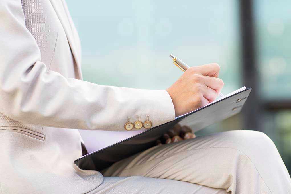 Shocking Parental Control Disrupts Job Interviews Person in beige suit writing on a clipboard.