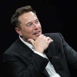 Pope’s SHOCKING Attack on Musk – Condemns Billionaire! Man in suit smiling, resting chin on hand.