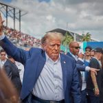 Assassin Challenges Trump To DEADLY Golf Match Person in blue suit waving at outdoor event.