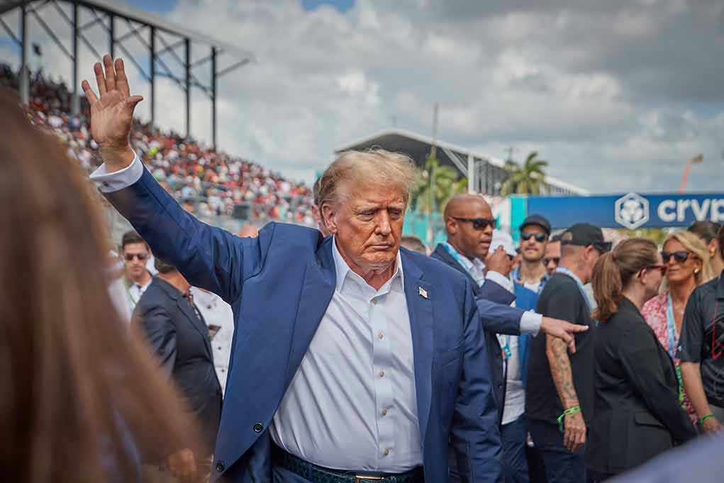 Assassin Challenges Trump To DEADLY Golf Match Person in blue suit waving at outdoor event.