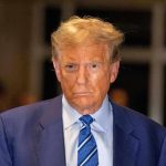 Trump–Epstein Statue SHOCKS DC – Who’s To Blame? Man in blue suit and striped tie, serious expression.