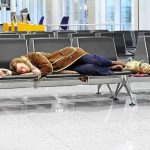Ransomware Shuts Down Major EU Airports – PASSENGERS STRANDED! A traveler sleeping on a bench in an airport waiting area