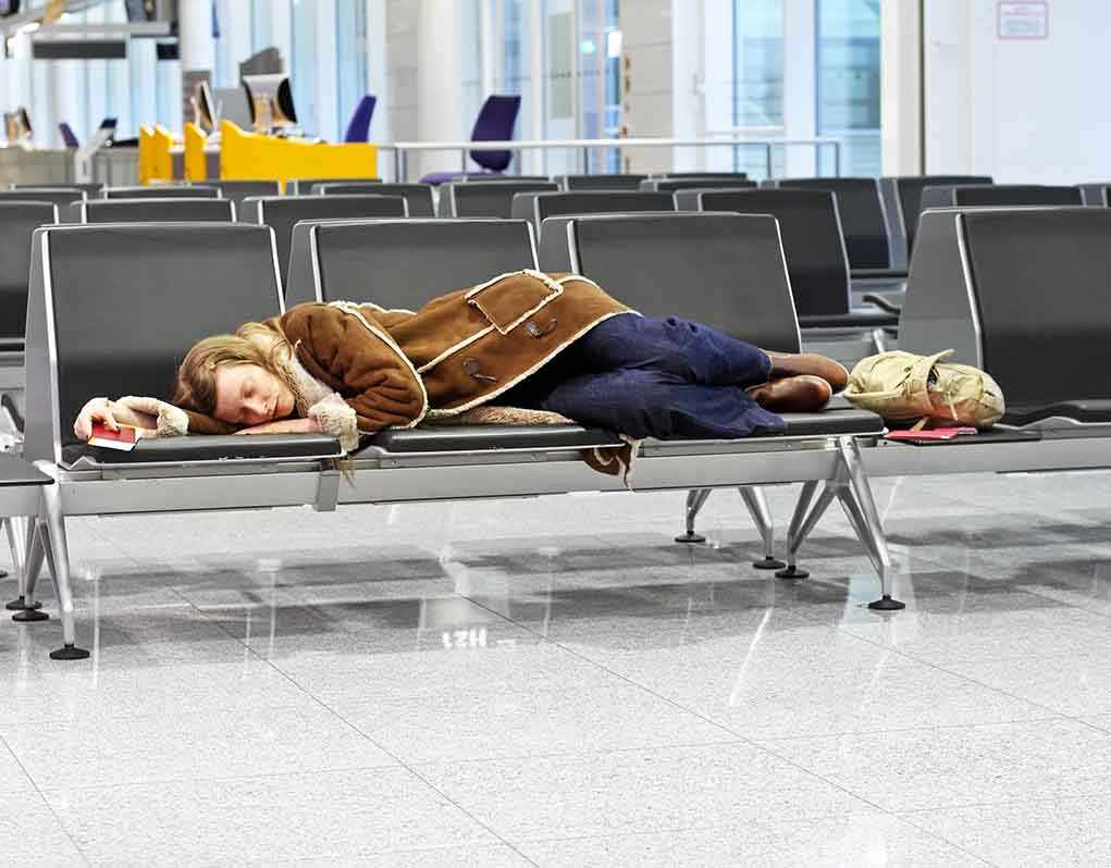 Ransomware Shuts Down Major EU Airports – PASSENGERS STRANDED! A traveler sleeping on a bench in an airport waiting area