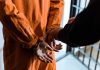 Neo-Nazis ARRESTED – Attack Plan THWARTED! Handcuffed person in orange jumpsuit being escorted.