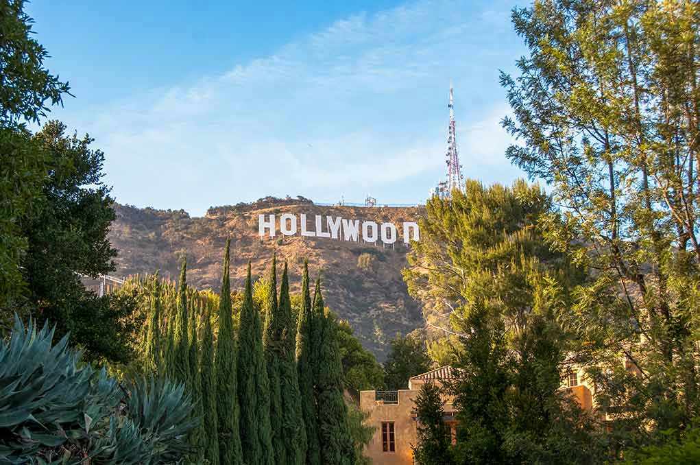 1164563563 Hollywood sign on hill surrounded by trees and buildings.