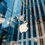 Apple CAVES — Succumb To Trump’s Pressure Apple store with glass facade and city reflections.