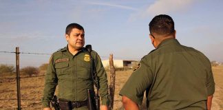 Two uniformed officers standing outdoors near a fence.