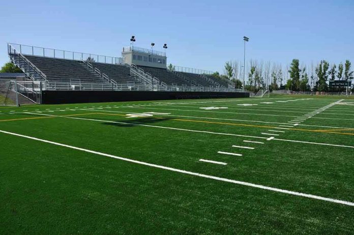 Empty football field with bleachers in background.