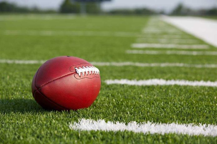shutterstock_160264247.jpg A red American football resting on a green artificial turf field