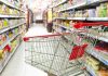 A shopping cart in a grocery store aisle filled with colorful products