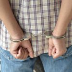 Massive Bar Bust: 249 ARRESTED! A person in handcuffs viewed from behind, wearing a plaid shirt and denim jeans