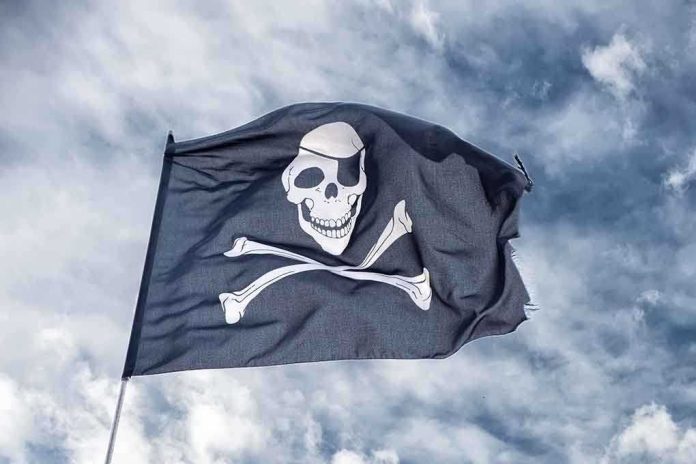 A black pirate flag featuring a skull and crossbones waving against a cloudy sky