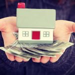 Homeowners BURNING Tax Bills – Fury Erupts Hands holding a small house model and cash bills