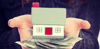 Hands holding a small house model and cash bills