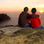 Wrong Text Creates LASTING Tradition A couple sitting on a cliff watching the sunset over the ocean