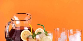 A pitcher of iced tea with lemon slices and mint, alongside glasses with ice and colorful straws