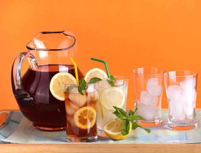 shutterstock_74696479.jpg A pitcher of iced tea with lemon slices and mint, alongside glasses with ice and colorful straws