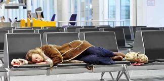 A traveler sleeping on a bench in an airport waiting area