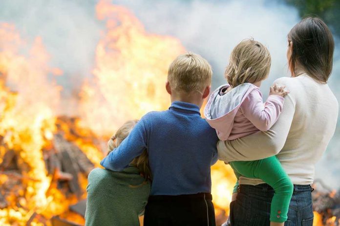 220431301. Three children and adult watching large fire outdoors