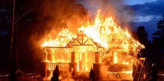 House engulfed in flames with firefighters present.