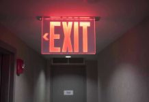 Teen Visitor KILLED in Stairwell Ambush Red illuminated exit sign in a hallway.
