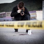Deputy MURDERS Son After Fentanyl Scandal Crime scene photographer behind police tape with evidence marker.