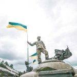 Soldier on tank holding Ukrainian flag.