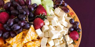 A colorful cheese and fruit platter featuring various cheeses and fresh fruits