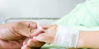 A person holding the hand of a patient with an IV in a hospital bed