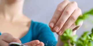 Person seasoning food with herbs from a pot