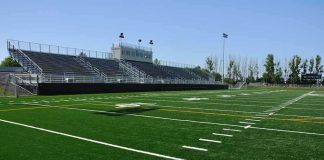 A football field with artificial turf and empty bleachers under a clear blue sky