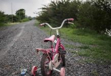 Pink childrens bike with training wheels on gravel path.