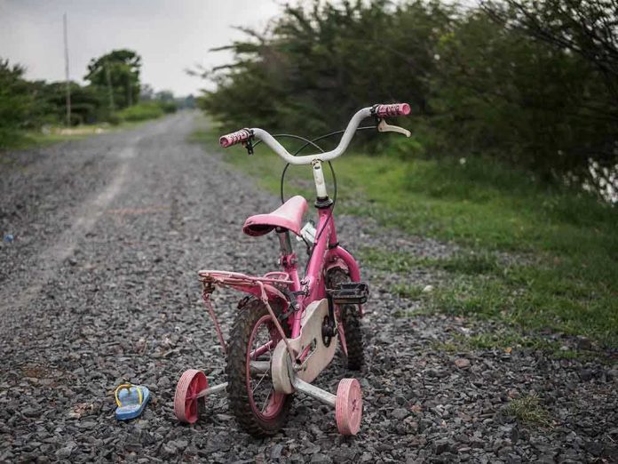 1098020117 Pink childrens bike with training wheels on gravel path.