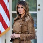 Woman in brown coat beside American flag.