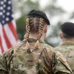 Soldier with braided hair in uniform, American flag visible.
