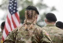 Soldier with braided hair in uniform, American flag visible.