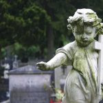 Weathered statue of a child angel holding a cross in a cemetery
