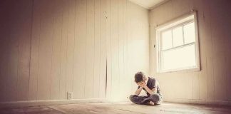 A child sitting alone in an empty room, covering their face with their hands
