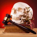 A skull, gavel, and scales of justice on a book against a dark background