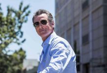 $90M Newsom Bailout: Taxpayers ROBBED Man in sunglasses wearing a blue button-up shirt.