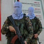 Masked soldiers holding rifles in front of a monument.