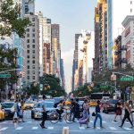 Busy city street with pedestrians, cars, and tall buildings.