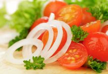 Close-up of sliced onions, cherry tomatoes, and green herbs on a wooden surface