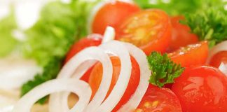 Close-up of sliced onions, cherry tomatoes, and green herbs on a wooden surface