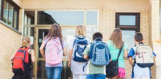 Group of children walking towards a school entrance with backpacks