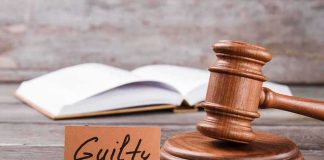 A wooden gavel next to a card that reads 'Guilty' and an open book